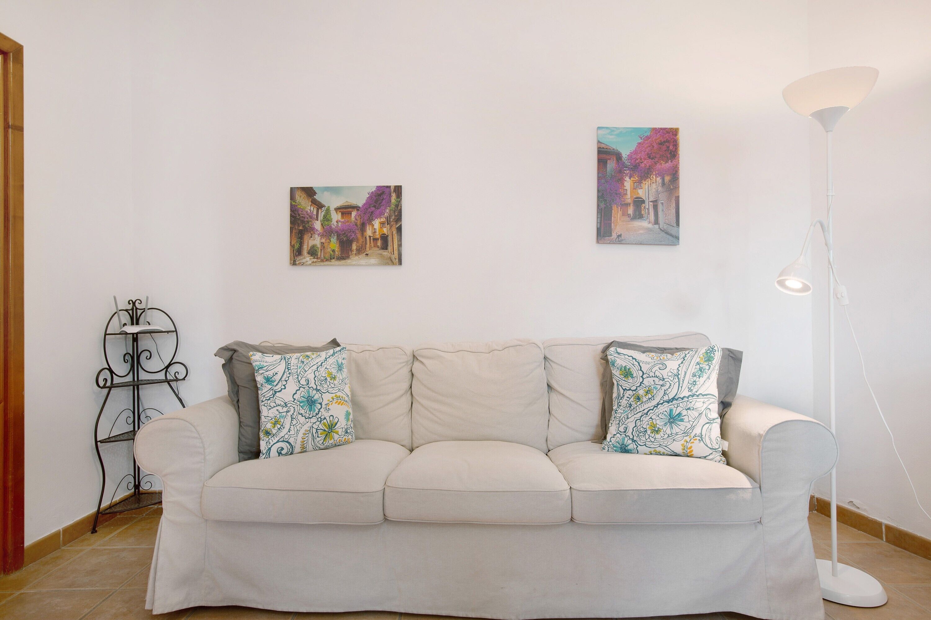 Un sofá de color neutro con cojines estampados, una lámpara de pie y dos cuadros en la pared.