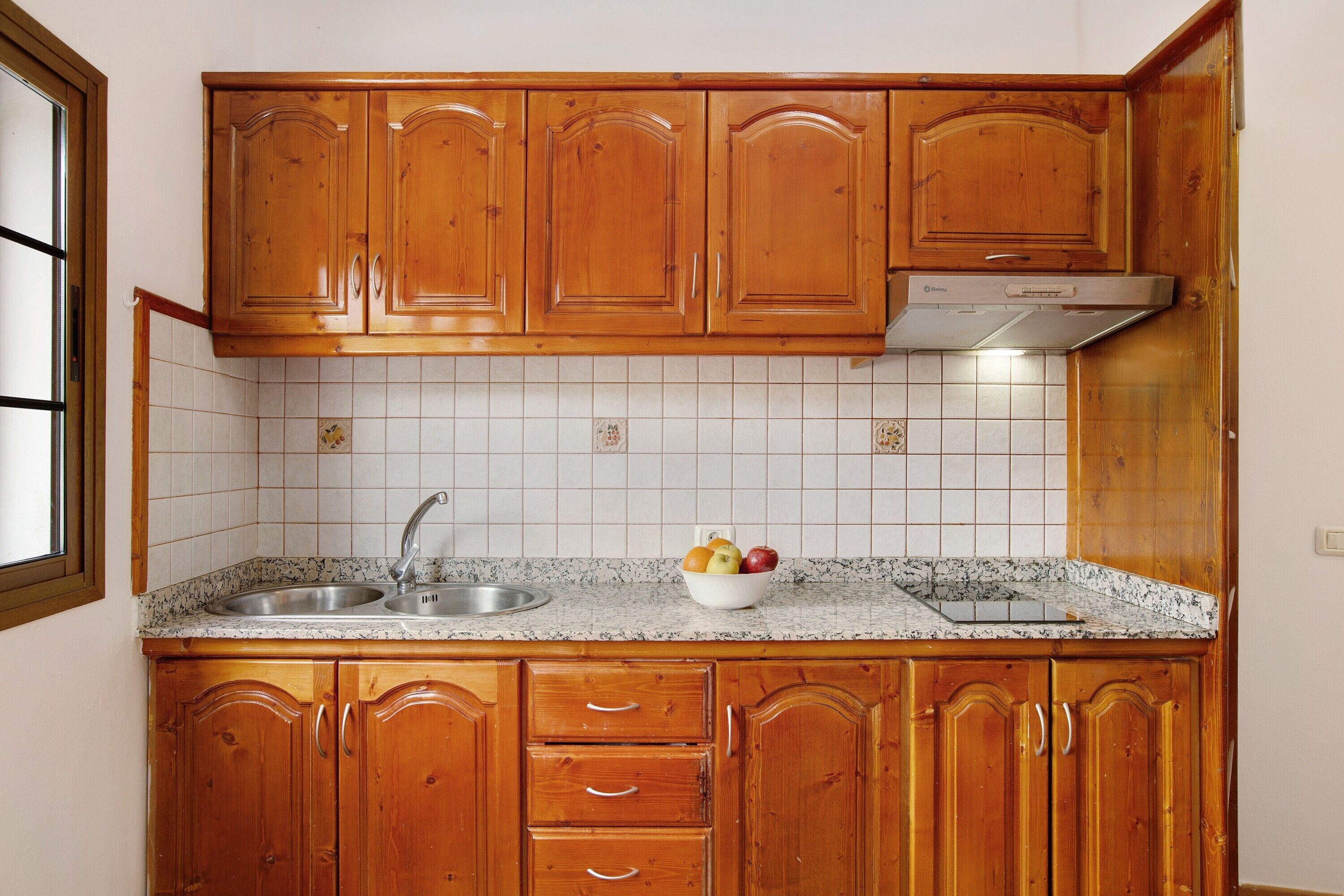 Una cocina con armarios de madera, un lavamanos de acero inoxidable y salpicadero de azulejos.
