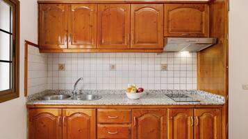 Una cocina con armarios de madera, un lavamanos de acero inoxidable y salpicadero de azulejos.
