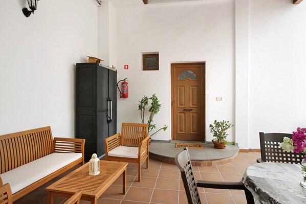 A room with a wooden sofa, two wooden chairs, a small table, a potted plant, a wooden door, and a fire extinguisher. - Holiday Home 'Cottage Santa Lucía 2' with Mountain View, Balconies & Wi-Fi (Santa Lucía de Tirajana)
