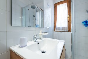 A bathroom with a white sink, a glass shower enclosure, and a window with blinds.