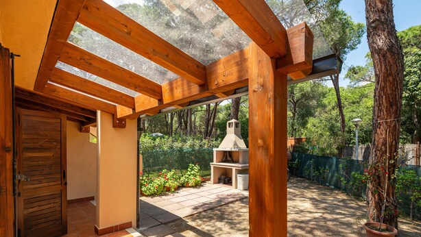 A covered patio area with wooden beams, a tiled floor, and a view of a forested area. - Holiday Home 'Villetta Pineta' with Private Garden (Santa Margherita di Pula)