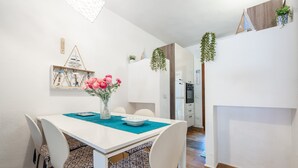 A dining area with a white table, patterned chairs, a vase of flowers, and a kitchen in the background. - Holiday Home 'Villetta Pineta' with Private Garden (Santa Margherita di Pula)