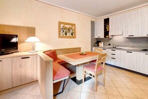 Une cuisine compacte comprenant un coin repas, des meubles de rangement en bois, un téléviseur et un tableau accroché au mur.