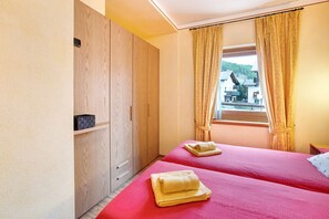 Une chambre d’hôtel avec deux lits, une armoire en bois, une fenêtre avec des rideaux et une vue sur un bâtiment à l’extérieur.