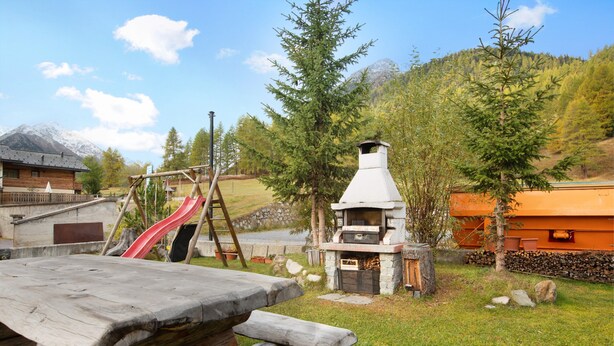 Eine rustikale Außenanlage mit einem Holztisch, einem Kamin aus Stein und einer roten Rutsche.
