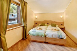 Un dormitorio con una cama de madera, dos almohadas, una ventana con cortinas y una mesita de noche.