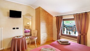 Un dormitorio con dos camas, un televisor montado en la pared, una mesita y una ventana con cortinas.