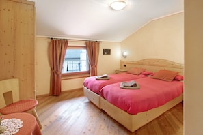 Ein Schlafzimmer mit einem hölzernen Bett, einem kleinen Tisch mit Untersetzer, einem Stuhl und einem Fenster mit Vorhängen.