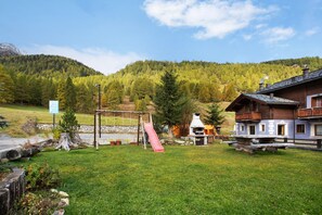 Ein Berghotel mit Spielplatz, Picknicktisch und Blick auf einen bewaldeten Berg.