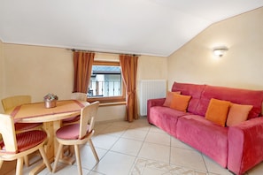 Ein Zimmer mit Esstisch, Stühlen, einem roten Sofa und einem fenster mit Vorhängen.
