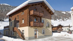 Un edificio de madera de varios pisos con balcones, una escalera y un techo cubierto de nieve.