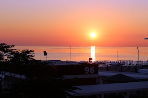 A sunset over a calm sea with a pier extending into the water. There are buildings with a sign displaying the number 96. - Hotel RECORD (Riccione)