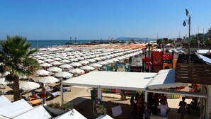 Una playa con numerosos sombrillas y sillas, cielo despejado y una vista distante del mar.