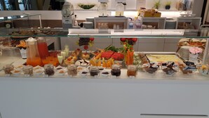 Un bufé con diversas opciones de comida y bebidas, entre ellas frutas, ensaladas y salsas.