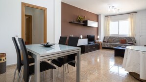 A modern living room with a dining table, chairs, a sofa, a TV, and a window with curtains.