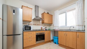 A kitchen with wooden cabinets, a stainless steel refrigerator, an oven, a microwave, and a blue trash bin.