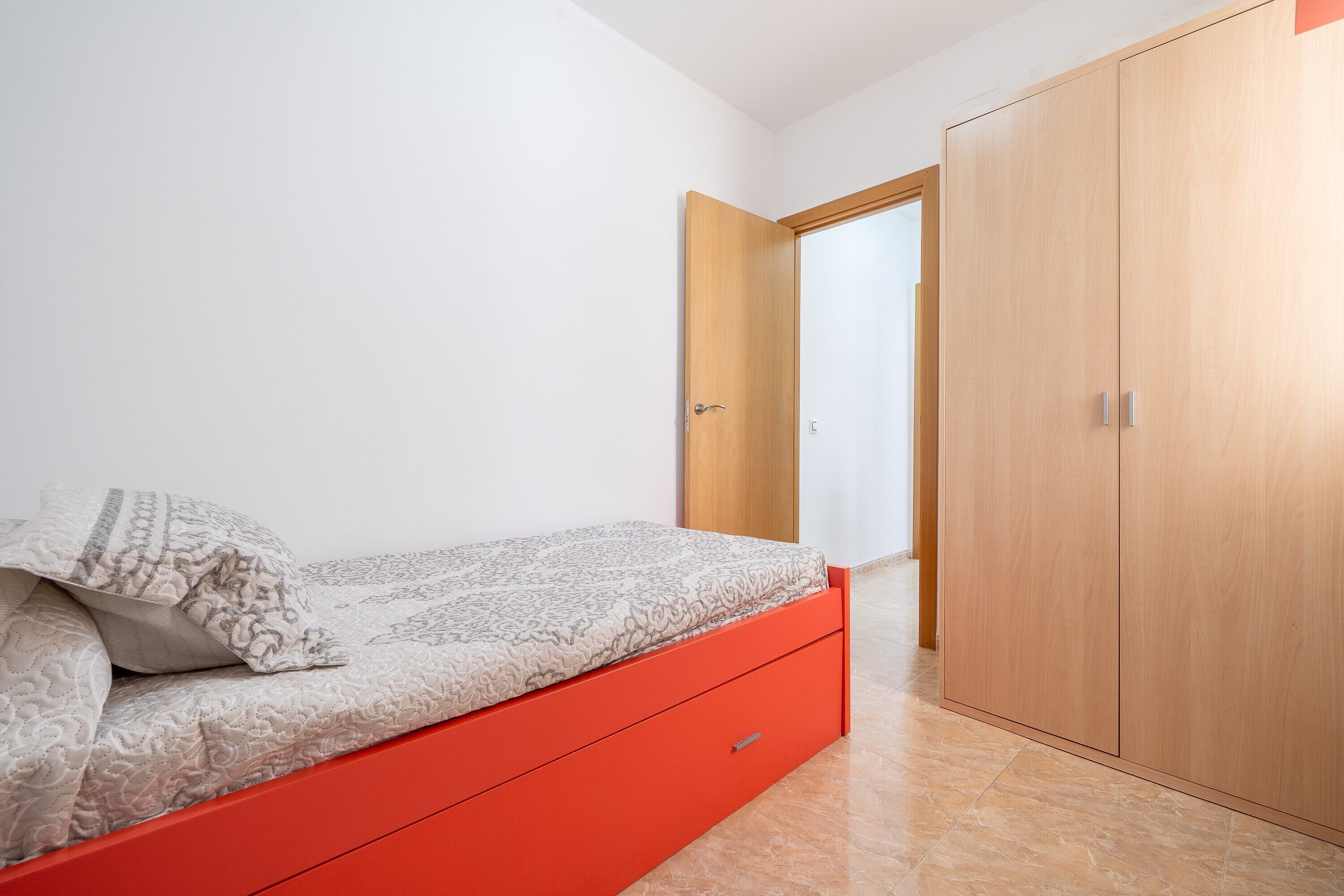 A bedroom with a bed, a red drawer, a wooden wardrobe, and a white door.
