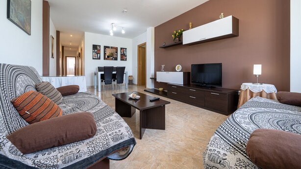 A living room with a sofa, coffee table, TV, and a dining area with chairs and a table.