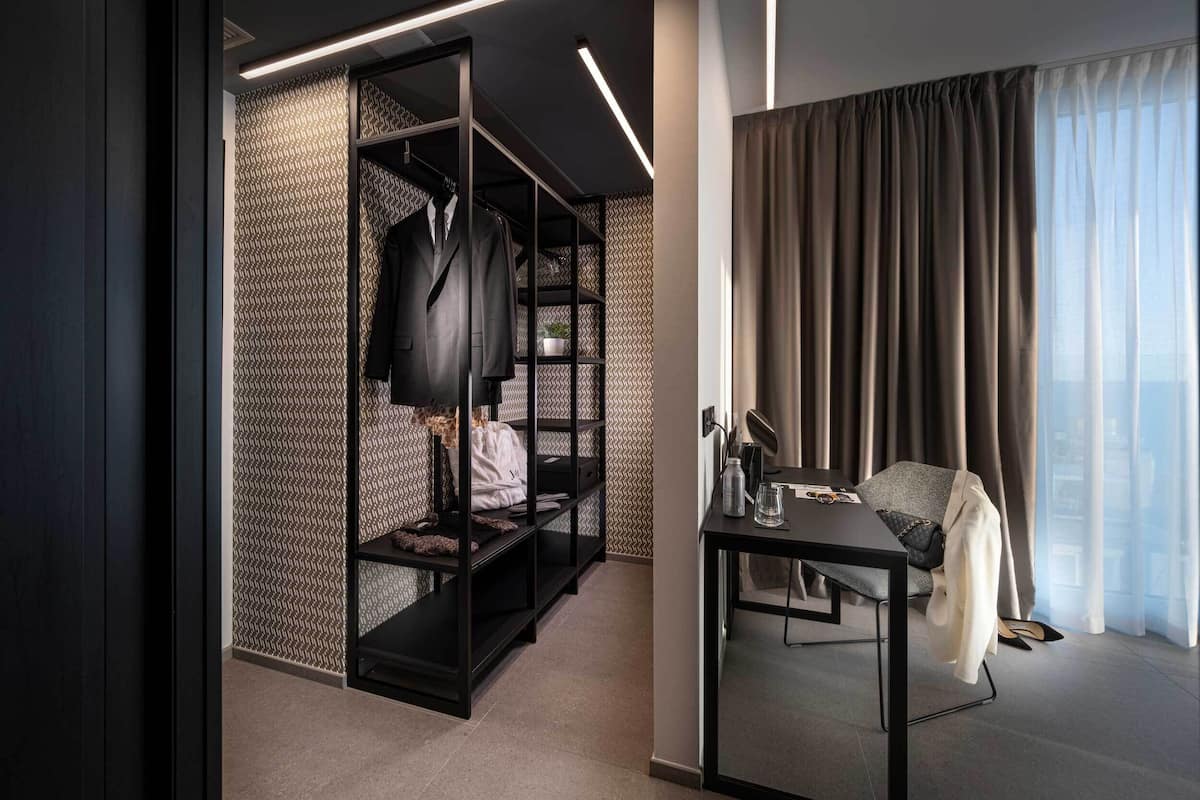 A modern hotel room with a built-in closet, a desk, and a large window with curtains.