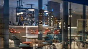A modern bar area with a city view through large windows, contemporary furniture, and a well-lit interior. - J44 Lifestyle hotel (Jesolo)
