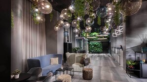 A modern interior with a sofa, chairs, and a coffee table, a hallway with a green wall, and hanging spherical lights. - J44 Lifestyle hotel (Jesolo)