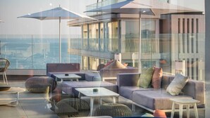 A modern rooftop lounge with comfortable seating, large umbrellas, and a glass balustrade overlooking the city. - J44 Lifestyle hotel (Jesolo)