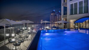An outdoor swimming pool with lounge chairs and umbrellas, surrounded by modern buildings. - J44 Lifestyle hotel (Jesolo)