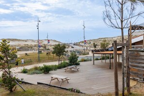 En strandpromenad med picknickbord, en träkonstruktion och utsikt över stranden och sanddynerna.