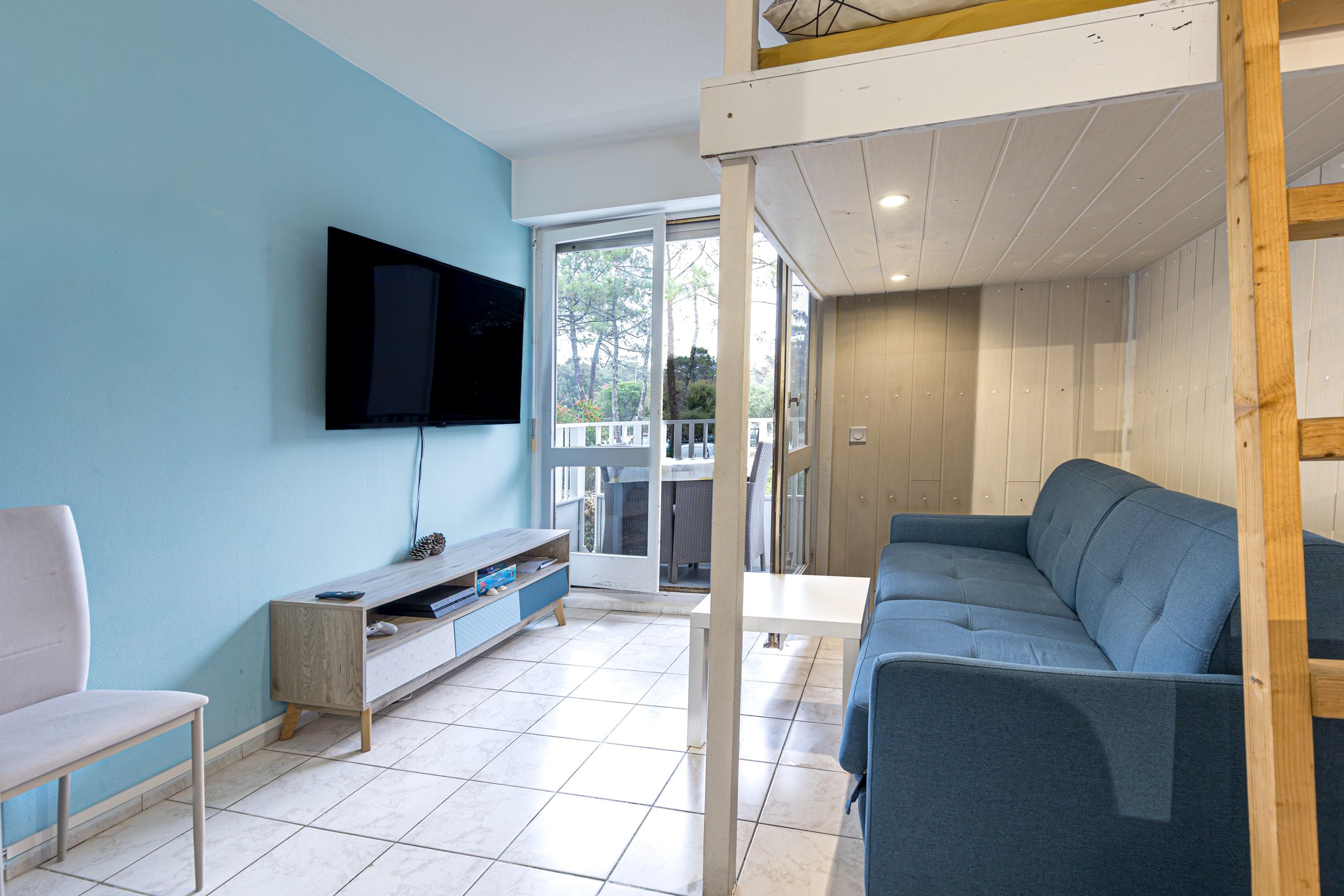 Una sala de estar con un televisor montado en la pared, un sofá, una mesita y un banco de madera.