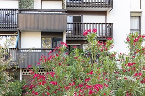 Ein mehrstöckiges Gebäude mit Balkonen, einem Garten mit roten Blumen und einer weißen Fassade.