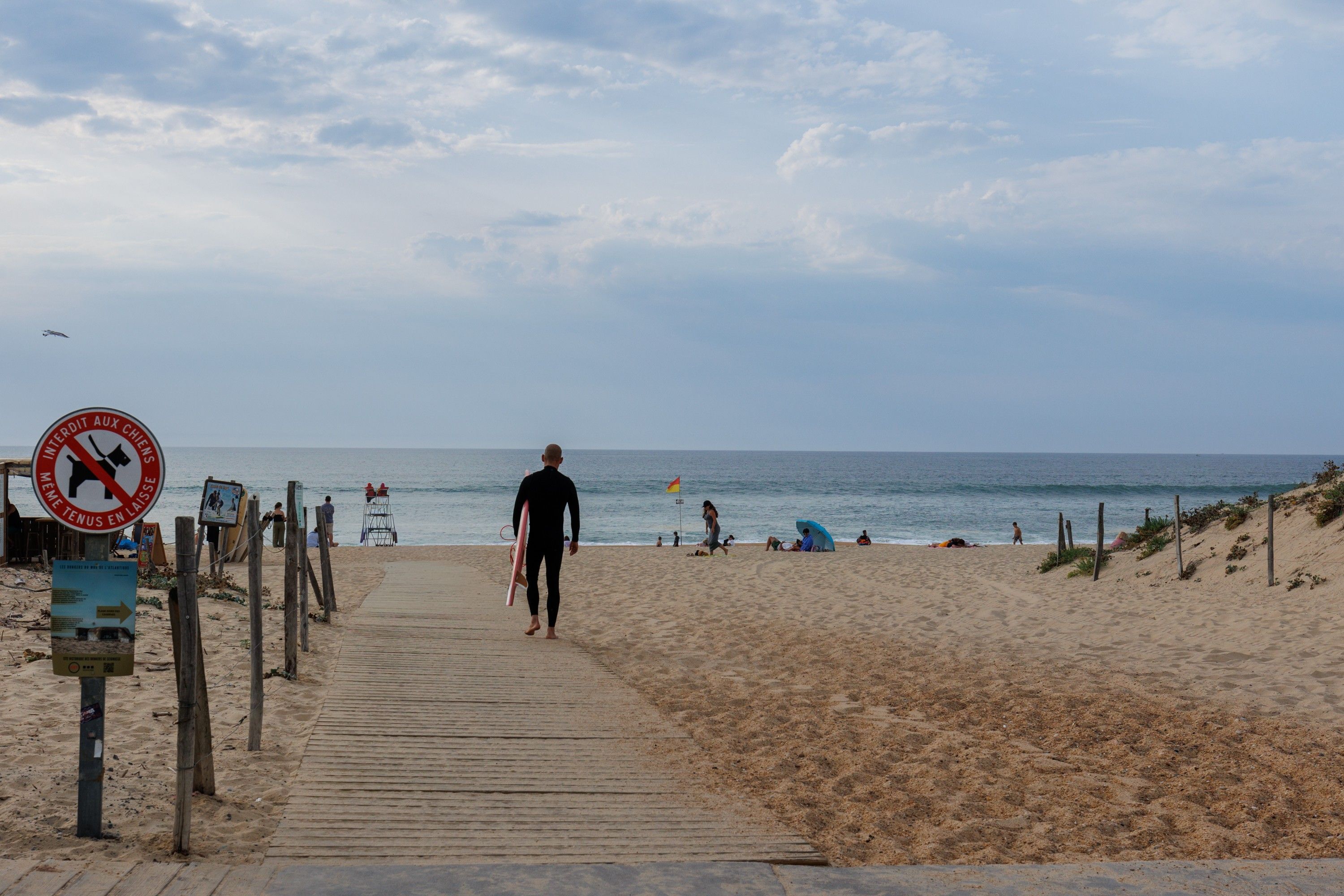 Ein Strand mit einer Holzpromenade, die zum Meer führt, einem Rettungsturm und einem Verbotsschild für Schwimmen.