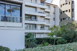 Un edificio residencial de varios pisos con balcones, un jardín con diversas plantas y un cielo despejado.
