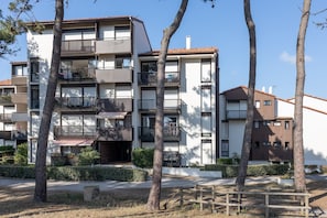 A multi-story residential building with balconies, a paved courtyard, and mature trees.
