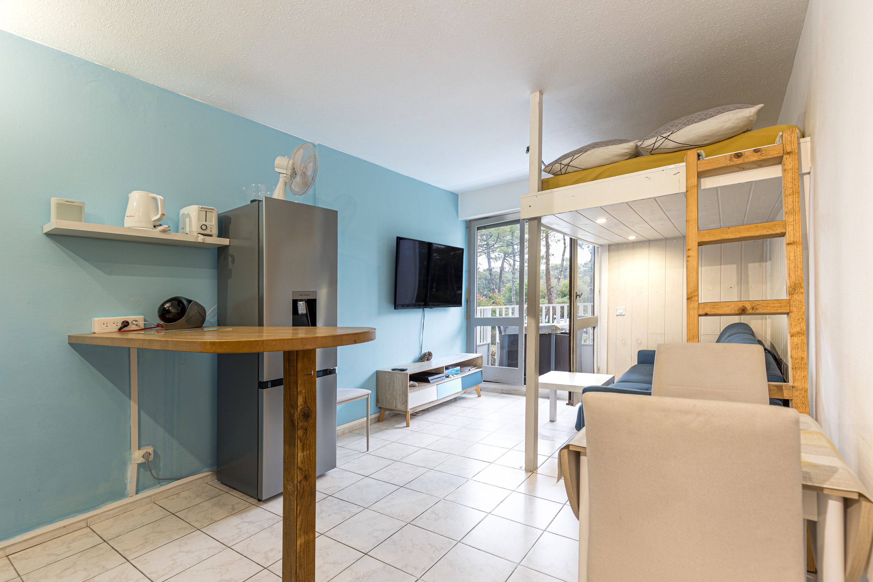 Un espacio habitable compacto con kitchenette, zona de comedor y dormitorio con cama en altillo.