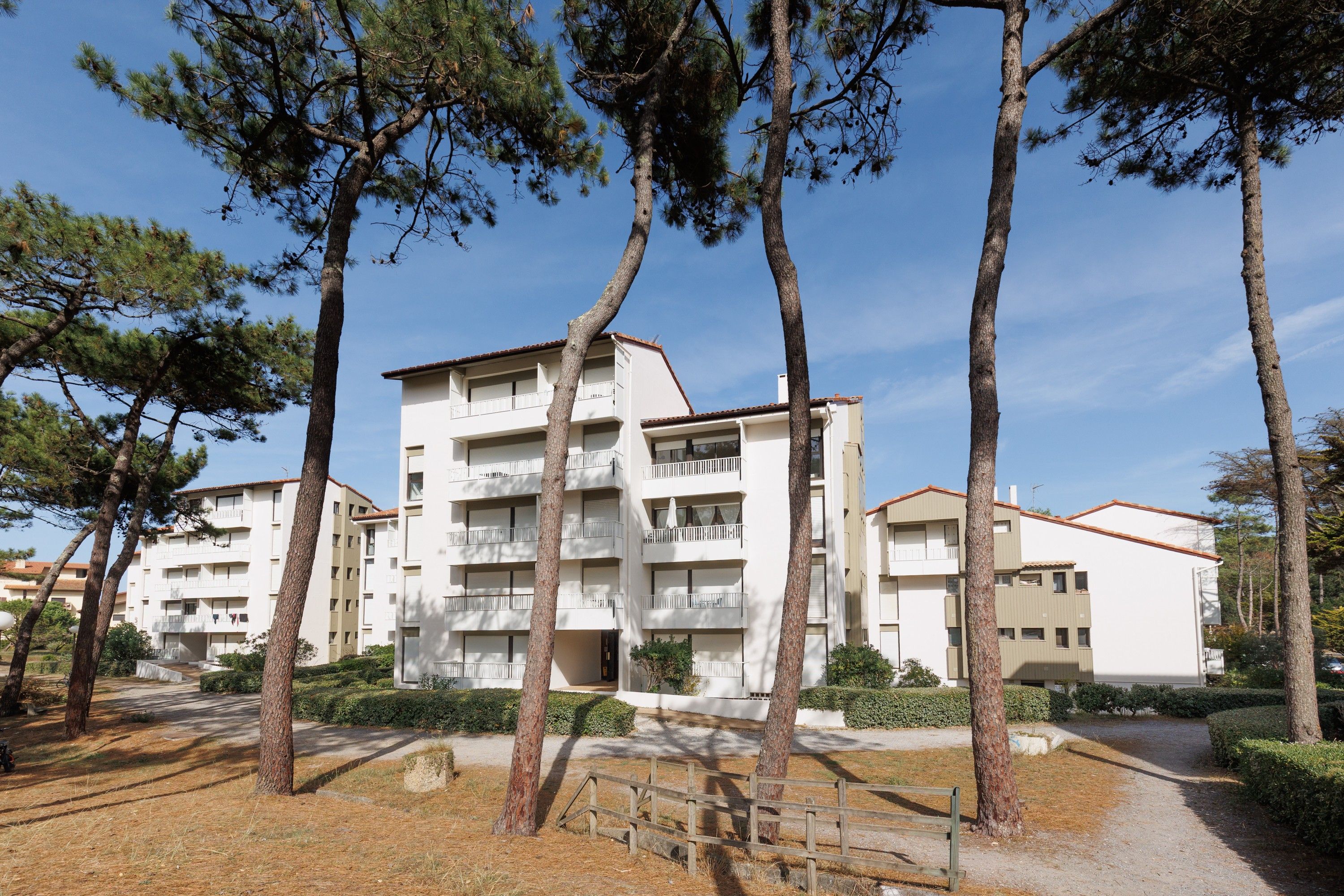 Un immeuble résidentiel à plusieurs étages, doté de balcons, entouré d’arbres et surplombant un ciel dégagé.