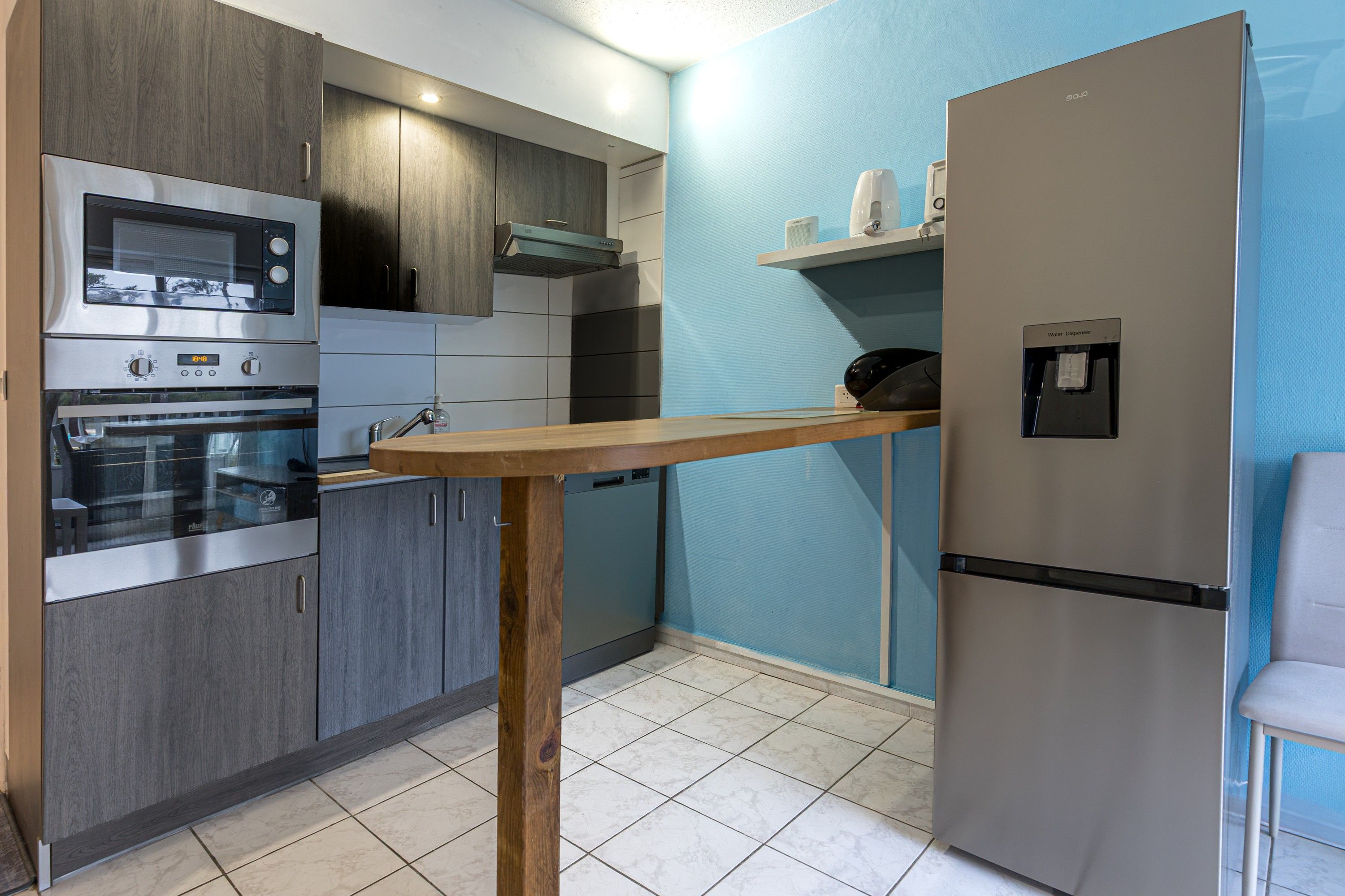 Una cocina moderna con electrodomésticos de acero inoxidable, una mesa de madera y un dispensador de agua.
