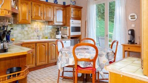 Een keuken met houten kastjes, een eettafel met stoelen, een koffieapparaat en uitzicht op groen.