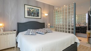 Een slaapkamer met een bed, nachtkastje, lamp en een wand met een ingelijst kunstwerk.