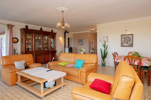 Un salon avec un canapé en cuir marron, une table basse en bois sur laquelle sont posées des partitions, une table à manger avec des chaises et un buffet aux portes en verre.