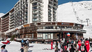 A multi-story hotel with balconies, ski equipment, and a snowy mountain backdrop.