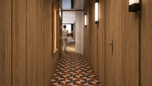 A hallway with wooden walls and a patterned floor, leading to a room with a bed and a window.