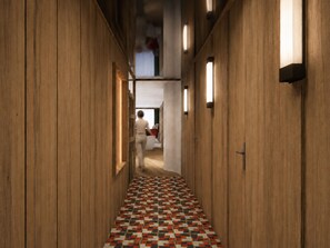 A hallway with wooden walls and a patterned floor, leading to a room with a bed and a window.