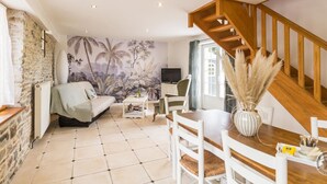 A cozy living room with a sofa, a dining table with chairs, a TV, and a mural on the wall.