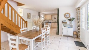A spacious dining area with a wooden staircase, white chairs, and a central table.