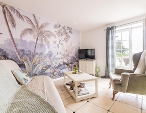 Ein Wohnzimmer mit einer großen Wandmalerei, einem Fernseher, einem Couchtisch und einem Sofa.