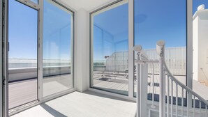 Un balcón amplio con puertas de cristal grandes, que ofrece una vista despejada de la playa y una barandilla blanca.