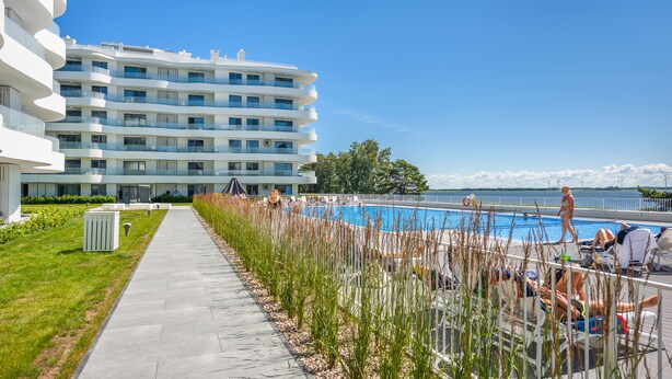 Un hotel moderno con zona de piscina, cielo despejado y vistas al agua.