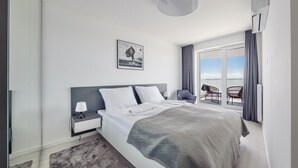 Habitación de hotel moderna con una cama grande, una mesita de noche, una silla y vista del cielo a través de una puerta corrediza.