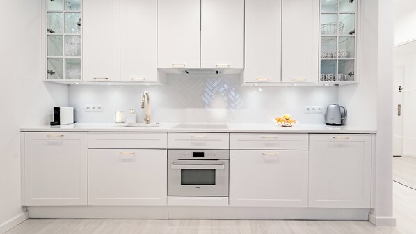 A modern kitchen with white cabinetry, a stainless steel oven, and a built-in range hood.